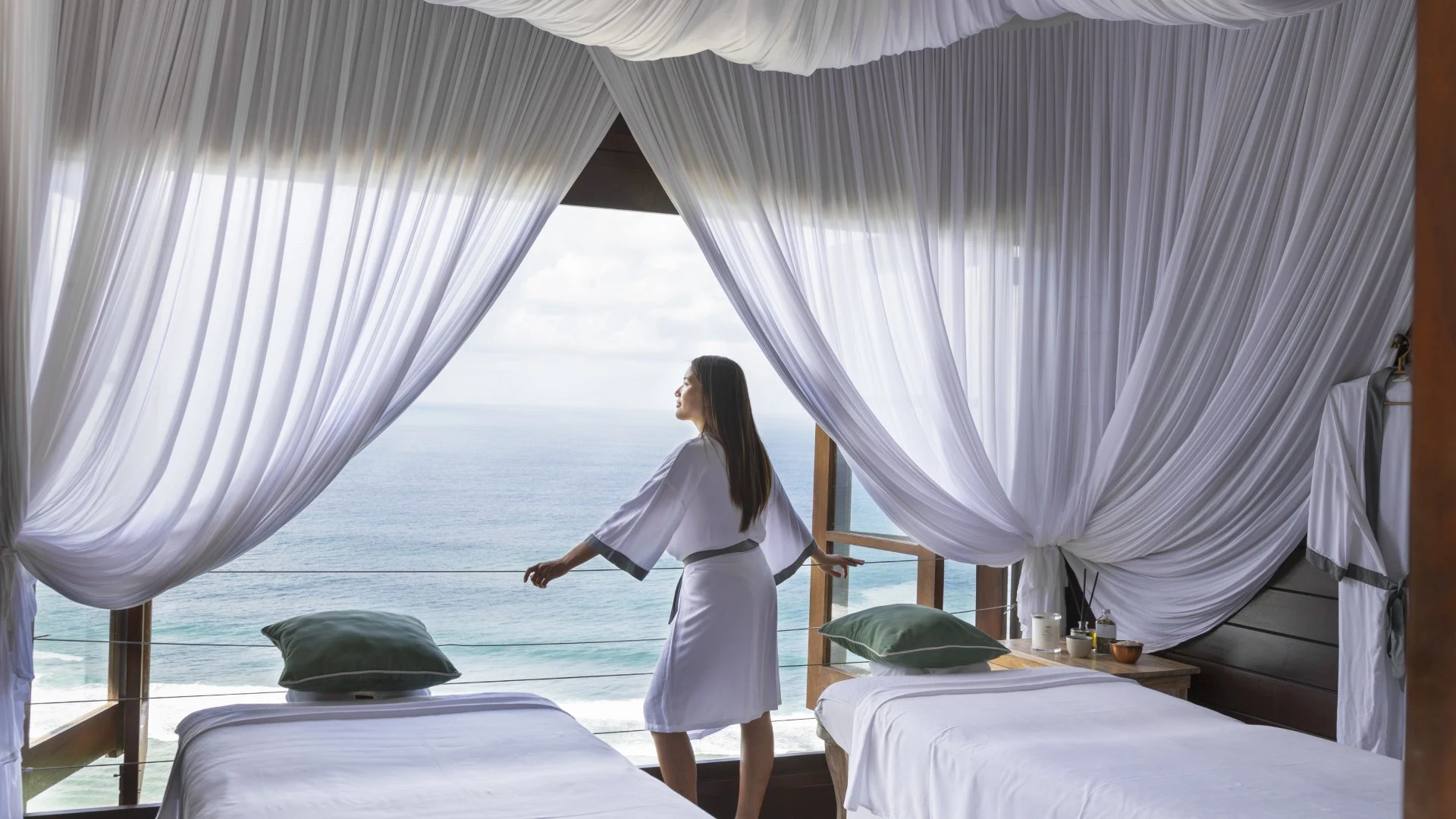 Woman in a white bathrobe looking out at the ocean view from a luxury treatment room at one of the best spas in Bali.