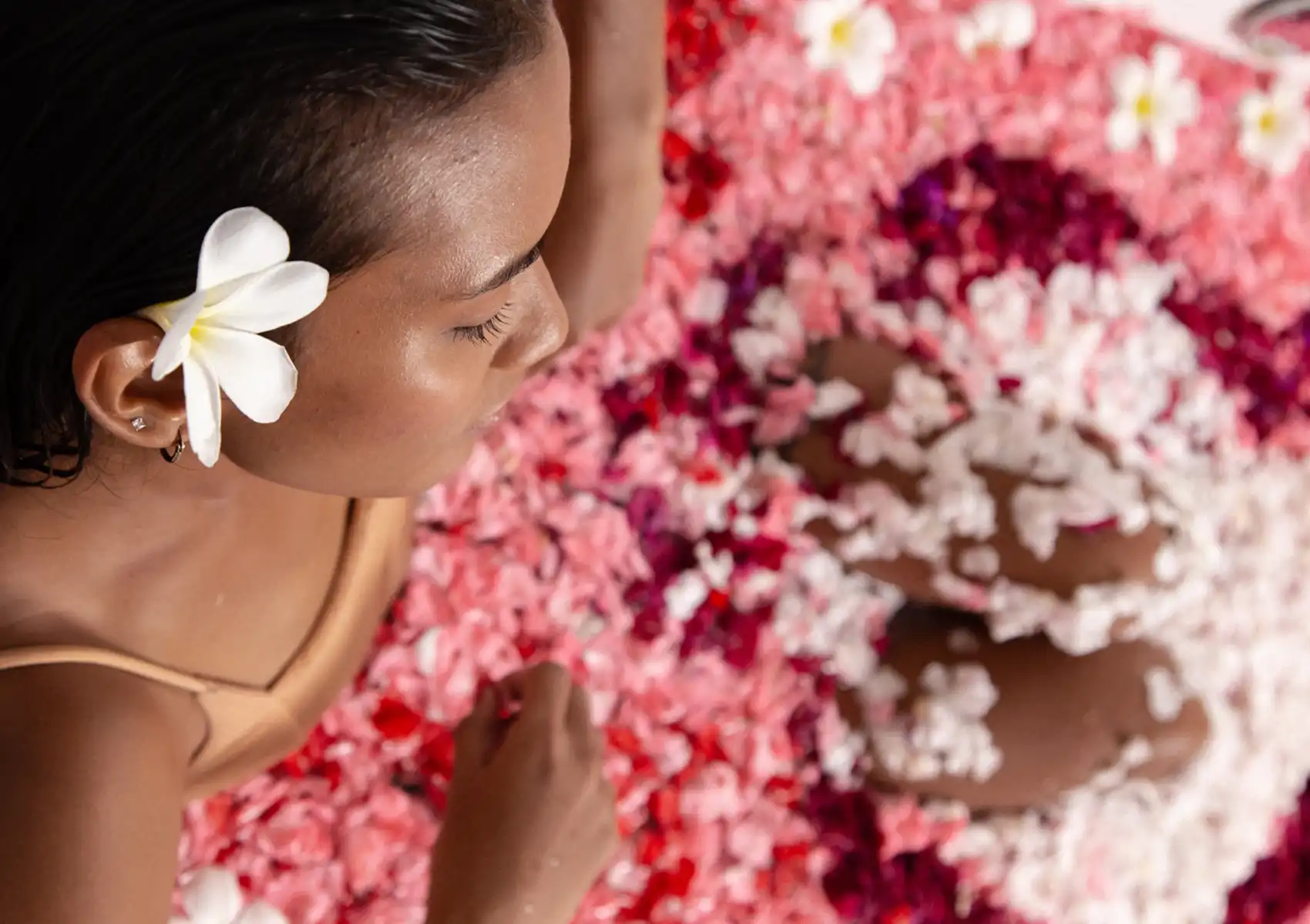 Spa for stress relief with person relaxing in flower petal bath, plumeria flower tucked behind ear.