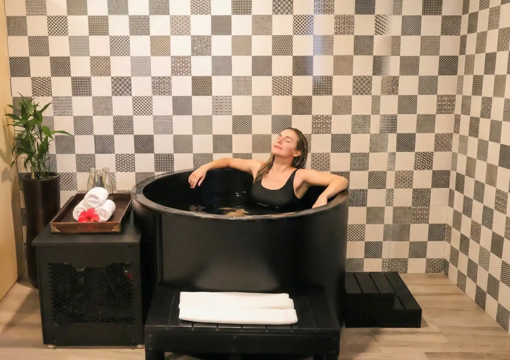 contrast-therapy-room Woman relaxing in a round black cold plunge tub in a spa room with monochrome checkerboard tile wall