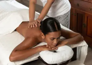 Woman lying face-down on a massage table receiving a back and shoulder massage from a therapist in white uniform at a Bali spa