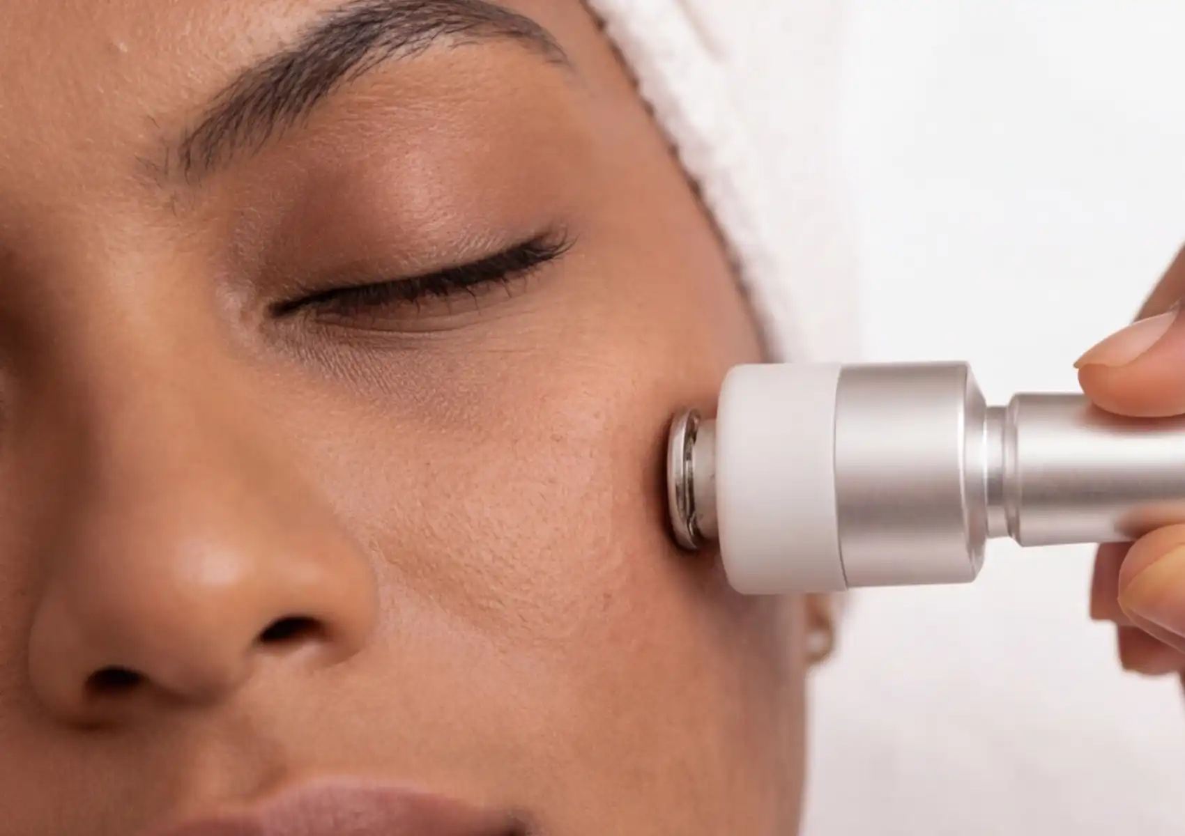 oxygeneo-facial-machine Close-up of an OxyGeneo facial device with a white and silver cylindrical tip being applied to a woman's cheek during a professional skin treatment