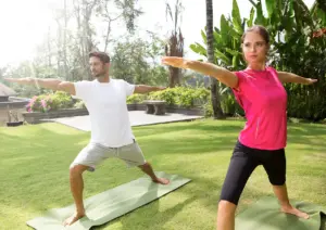 Yoga and spa retreat Bali — two people in a standing yoga pose outdoors on mats, surrounded by tropical greenery.