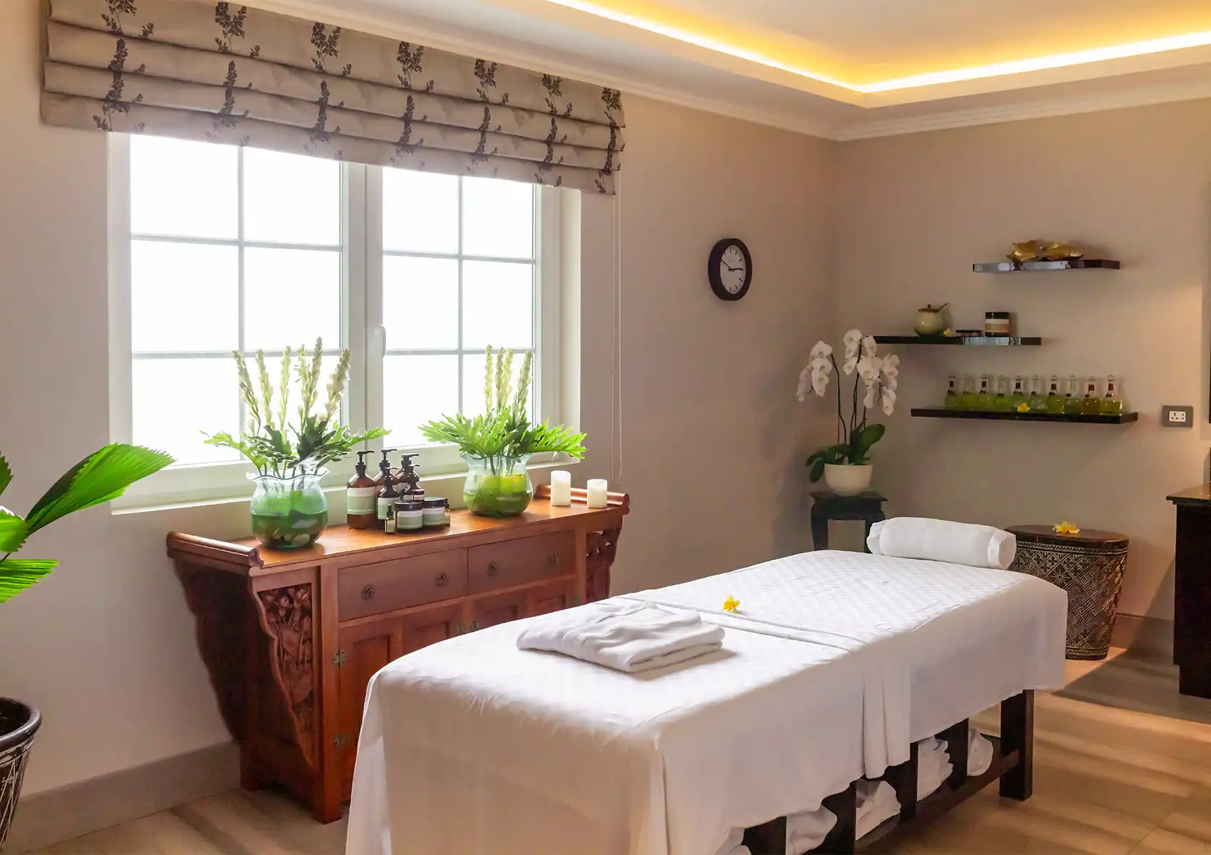 facial-treatment-akoya-spa A serene, well-lit spa room featuring a comfortable white treatment bed, elegant floral arrangements, and a wooden cabinet displaying premium skincare products, providing the perfect environment for advanced facial treatments Ubud.