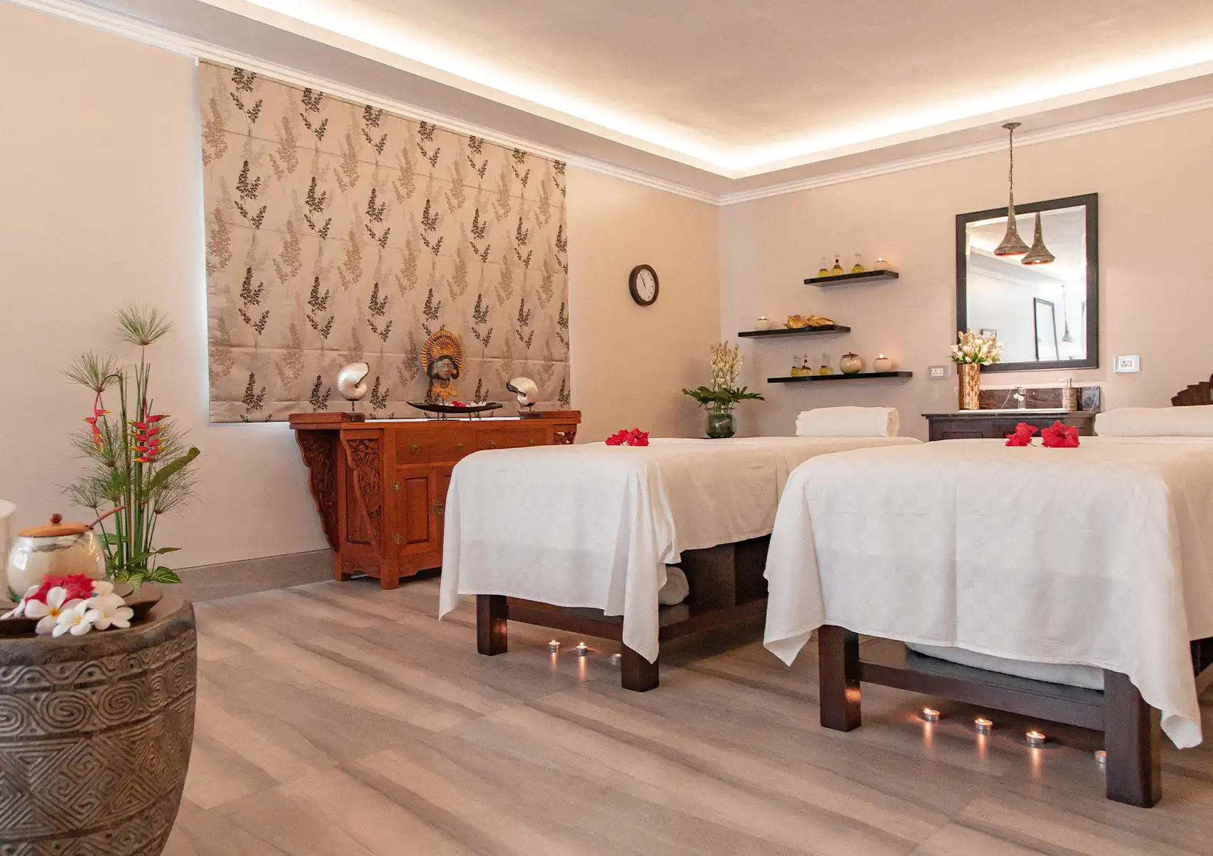 A serene couples massage room featuring two beds adorned with red flowers and fresh linens, prepared for guests at a spa in Ubud.