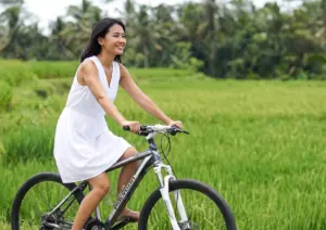 A woman happily riding a bicycle past vibrant green rice fields, combining local outdoor activities with a visit to the best spa in Ubud.