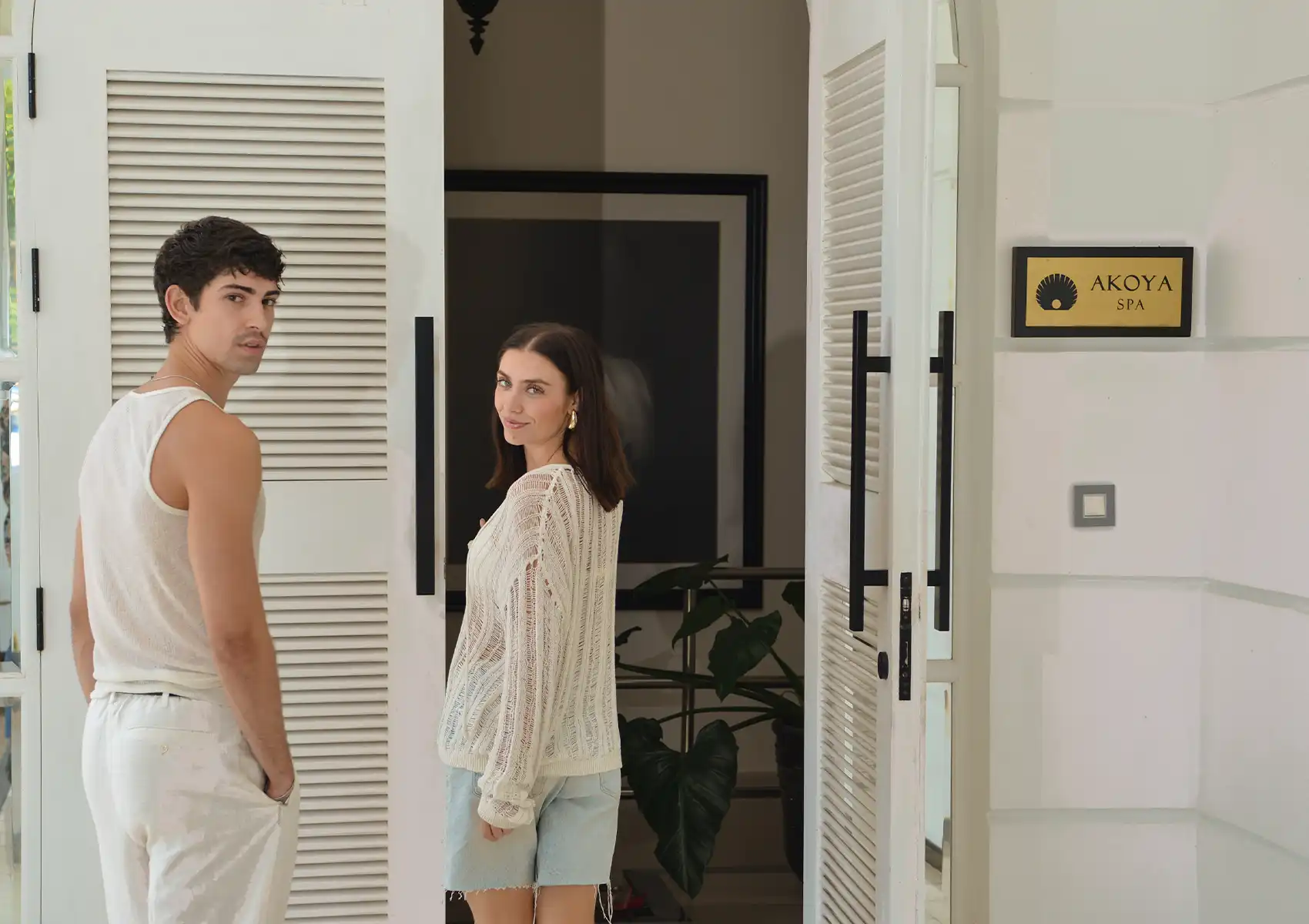 A casual couple smiling as they walk through the open white louvered doors of Akoya Spa, a welcoming day spa in Ubud.