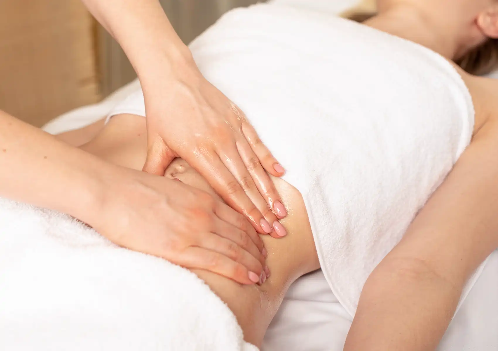 Close-up of a therapist performing a soothing abdominal massage with oil on a draped client at a spa in Ubud.