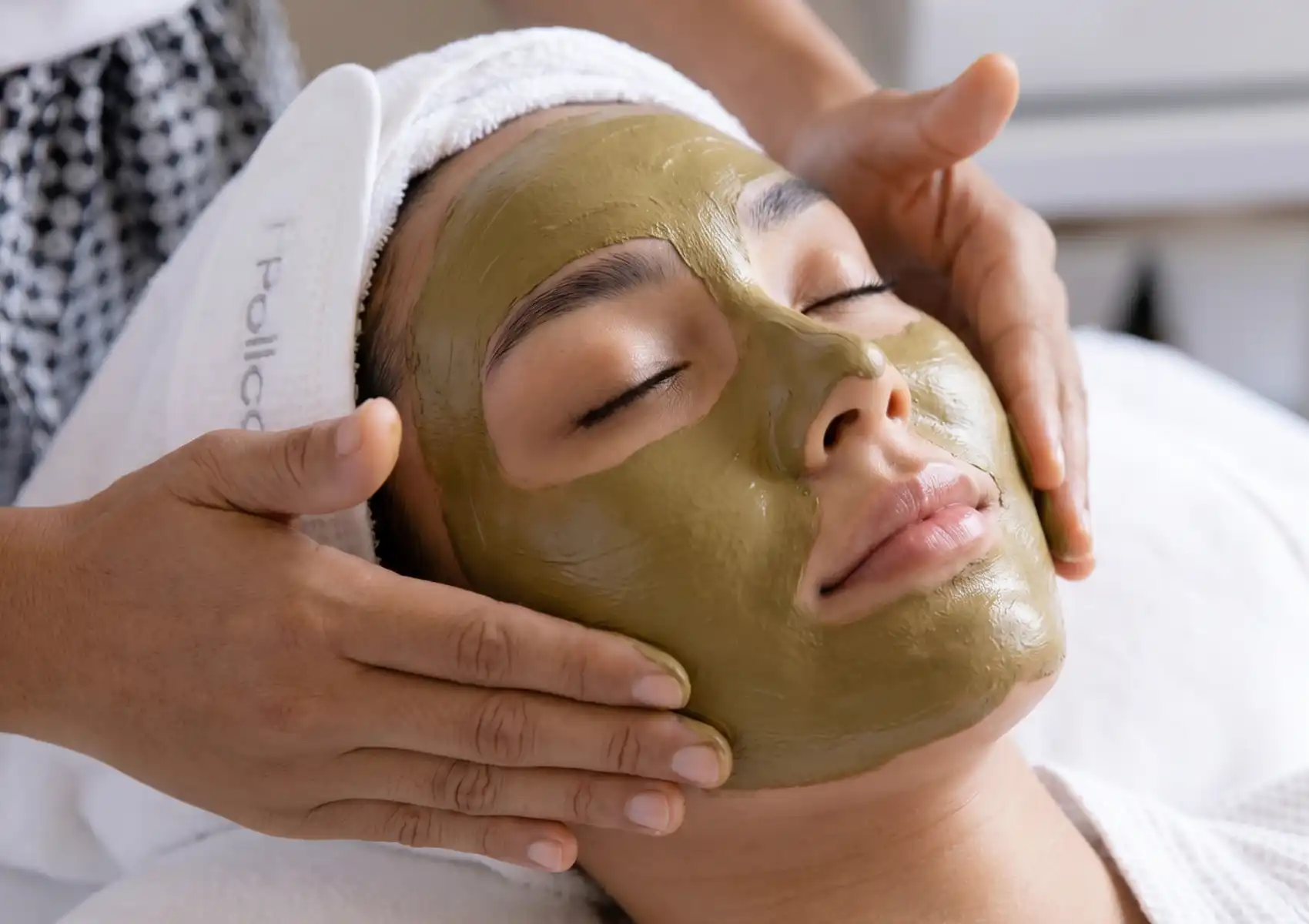 Close-up of a relaxed woman with her eyes closed as a spa therapist gently applies a soothing green facial mask during a microdermabrasion treatment in Ubud.