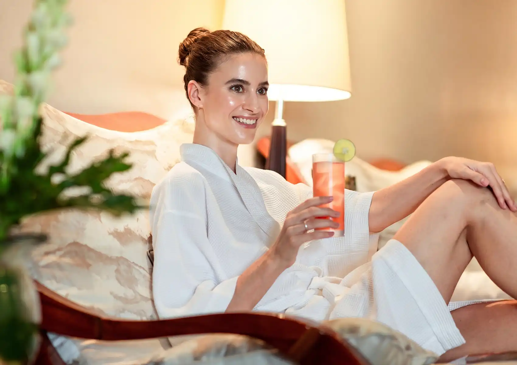 skin-resurfacing-treatment A smiling woman in a white spa robe relaxes on a lounge chair holding a refreshing pink iced drink after a microdermabrasion skin-resurfacing treatment.