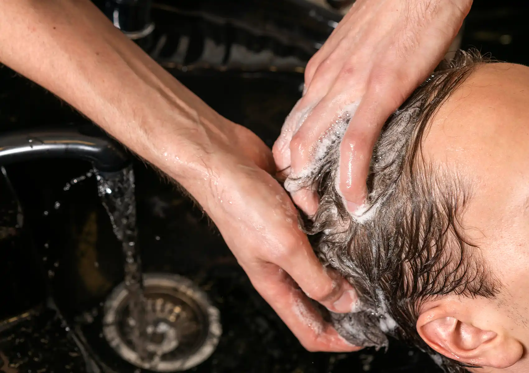 Close-up of a therapist's hands massaging a soapy lather into a client's scalp at a washing basin during a rejuvenating hair treatment at a spa in ubud.