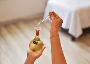 A therapist's hands using a glass dropper to extract aromatic rose massage oil from an elegant round bottle inside a tranquil treatment room at the Best spa in Ubud.