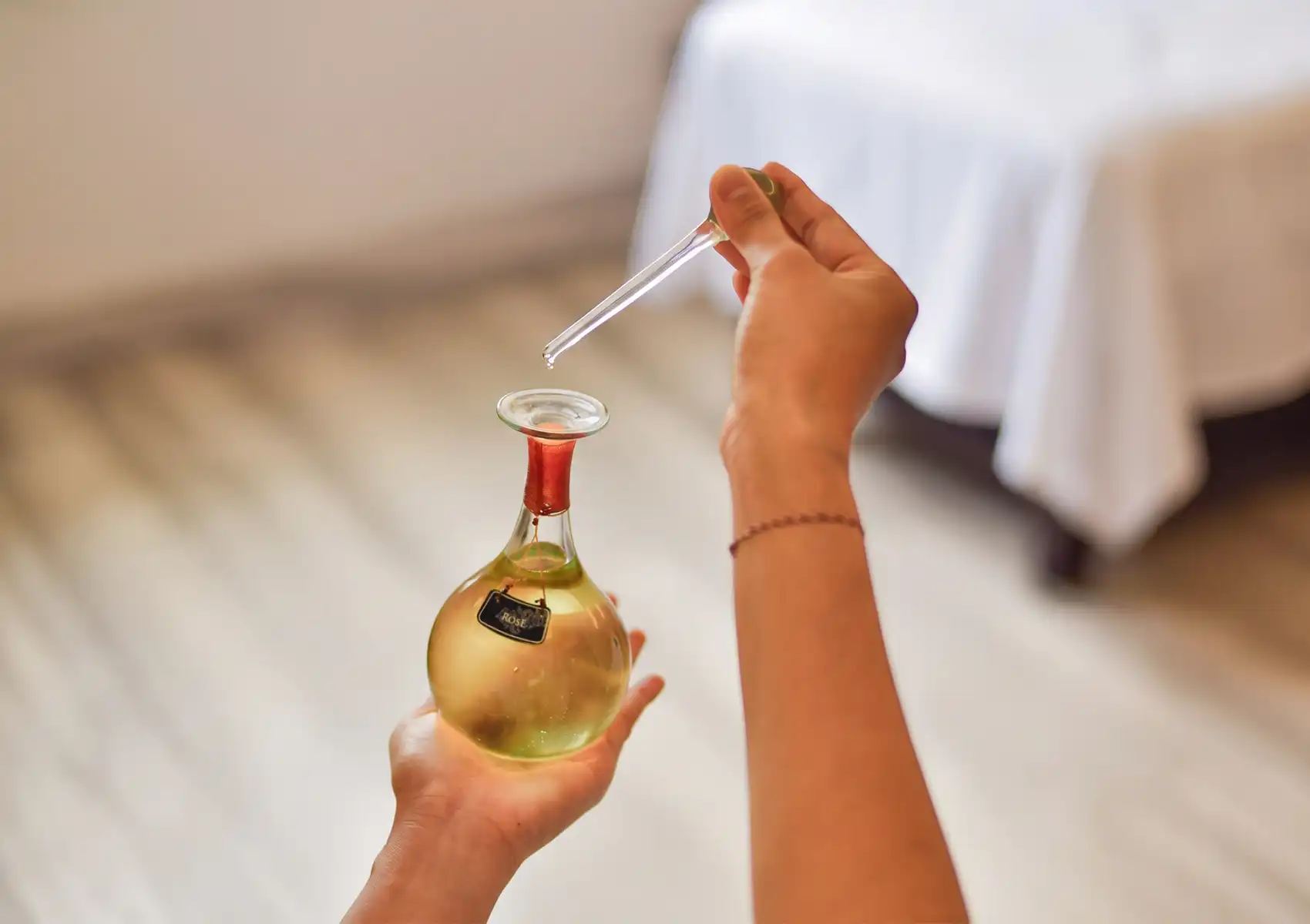 A therapist's hands using a glass dropper to extract aromatic rose massage oil from an elegant round bottle inside a tranquil treatment room at the Best spa in Ubud.