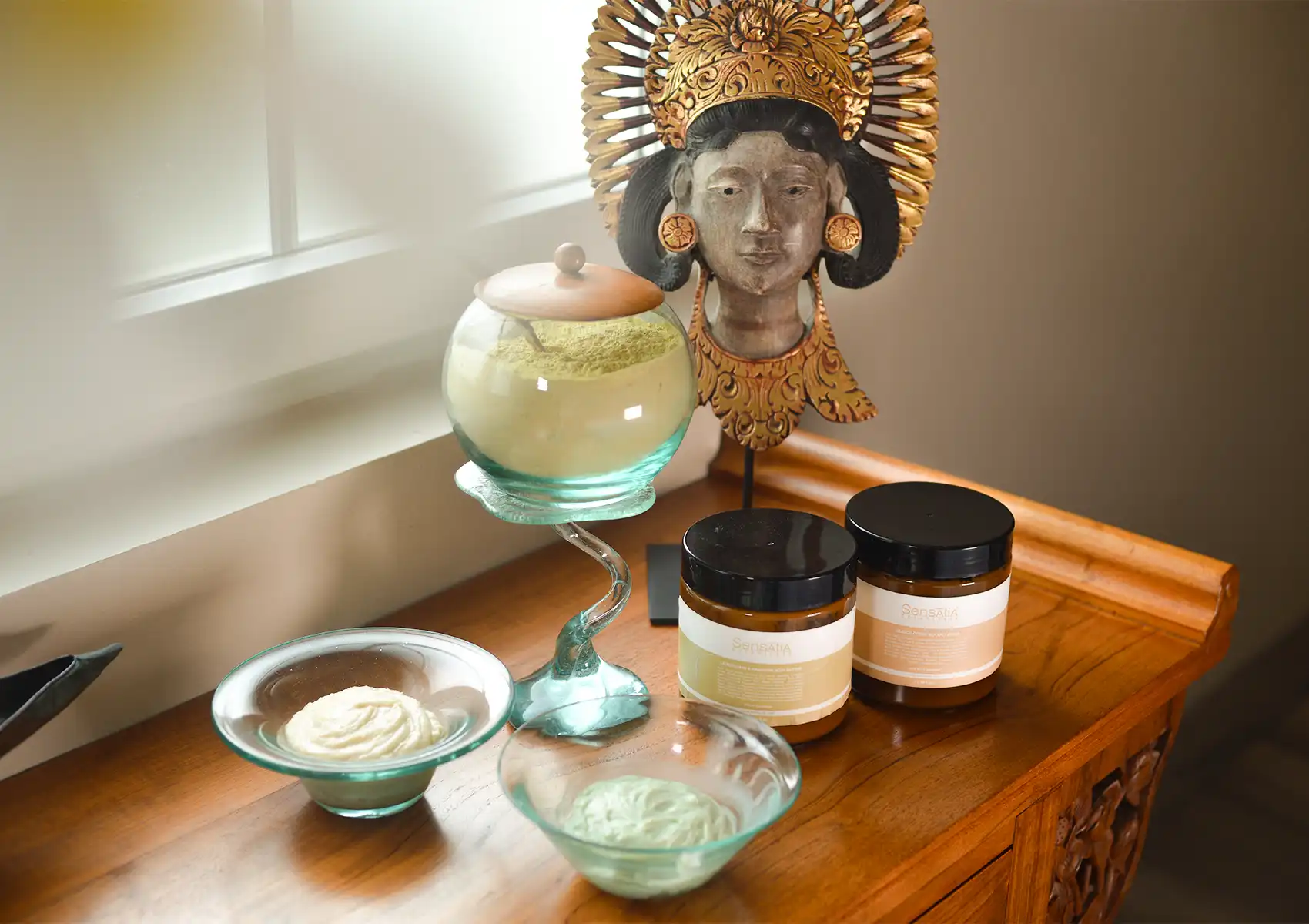 A display of natural spa ingredients, including botanical powders and essential oils, arranged beautifully on a wooden table beside a traditional Balinese statue at the best spa in ubud.