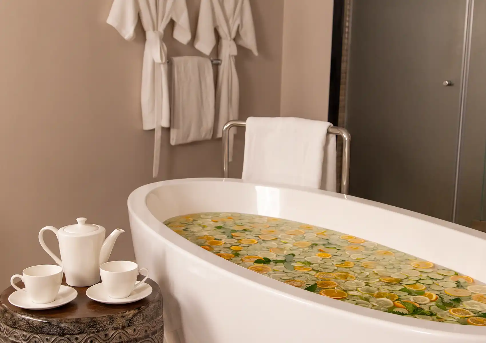 A freestanding white bathtub filled with water, sliced citrus fruits, and leaves, set up next to a tea service for a luxurious soak at the best spa in ubud.