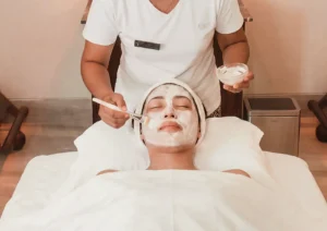 A professional esthetician carefully applying a nourishing white facial mask with a soft brush to a relaxed client lying on a treatment bed, an ideal dry season skincare treatment at the best spa in ubud.