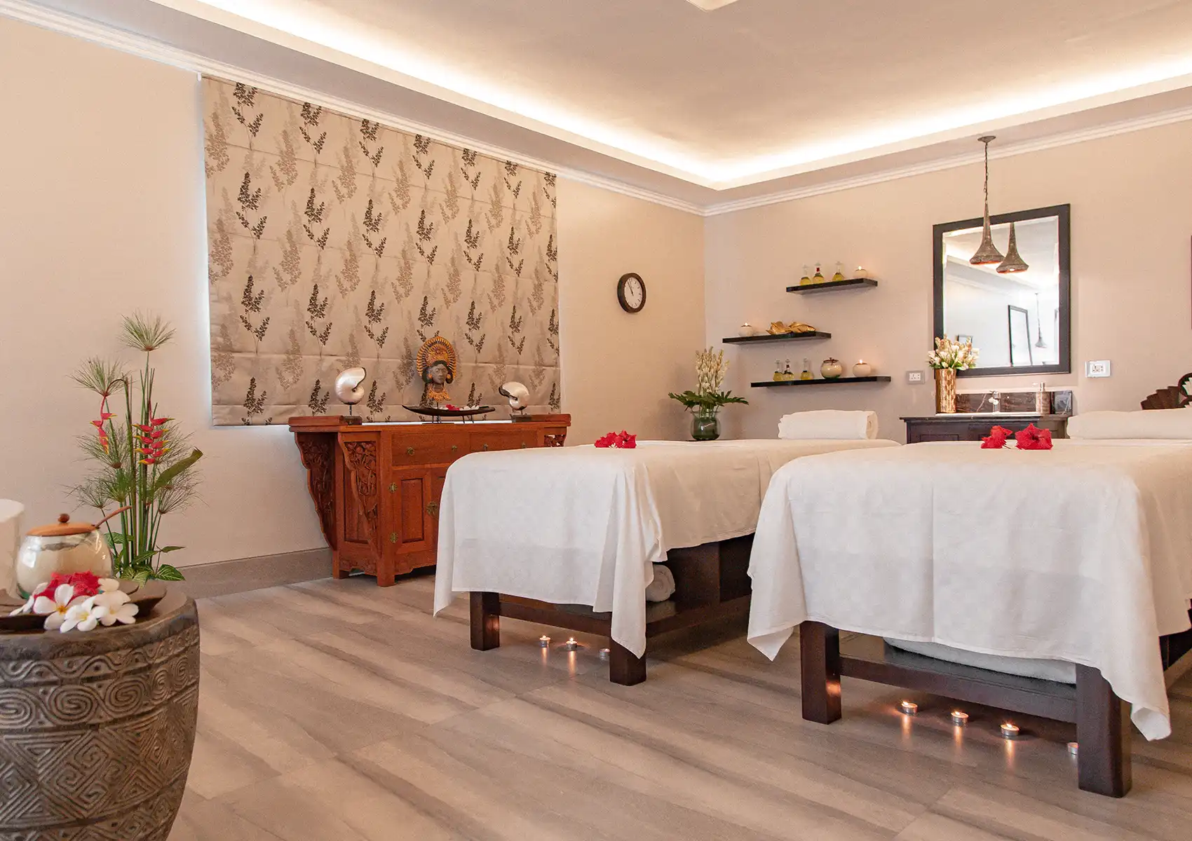 A tranquil couples treatment room featuring two massage beds adorned with red flowers, traditional Balinese decor, and ambient floor candles at the best spa in ubud.
